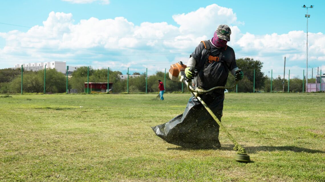 Trabajador desbroza un campo deportivo durante labores de mantenimiento en Ciénega de Flores