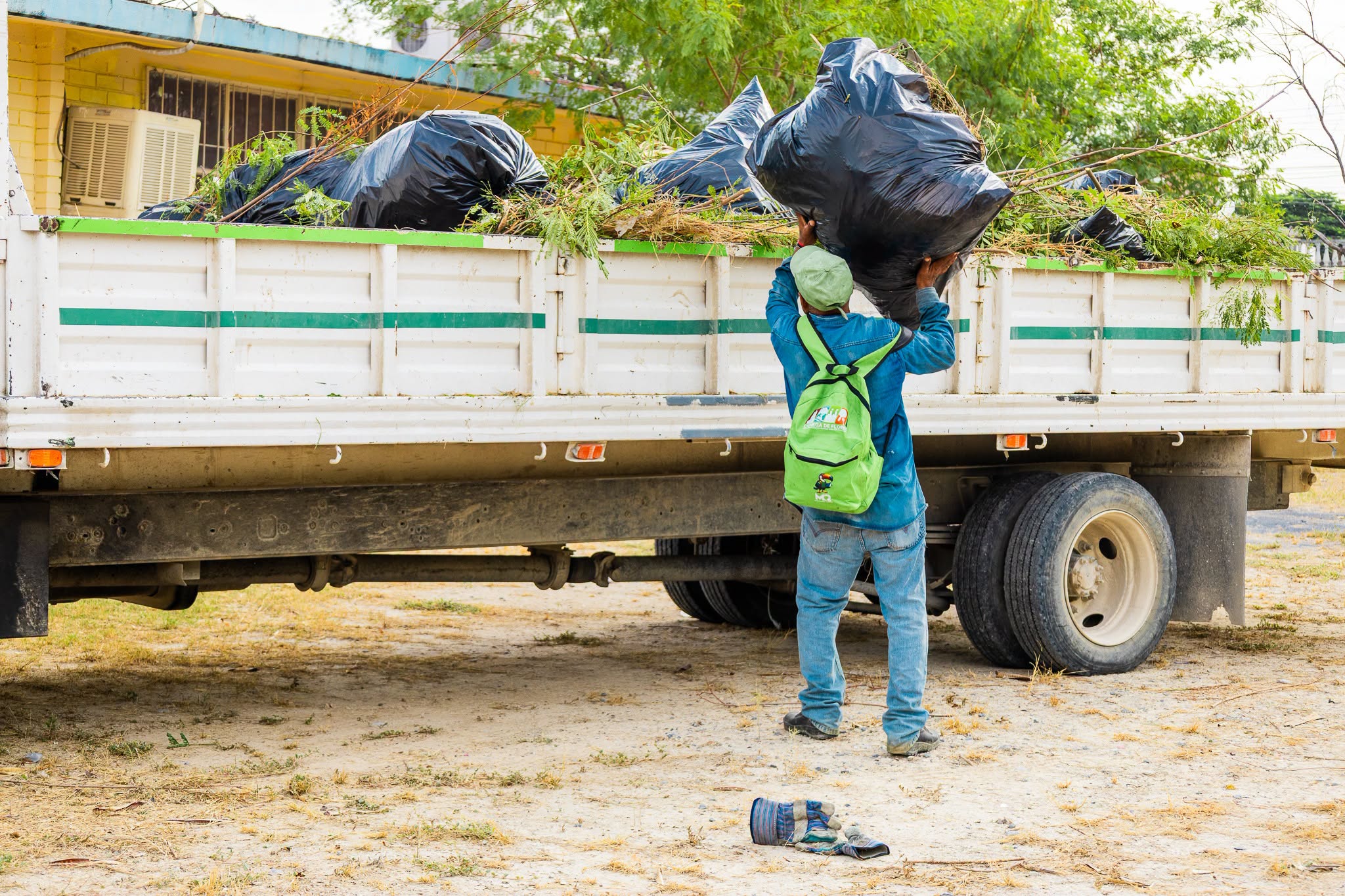 Participante en la limpieza carga una bolsa en una camioneta con ramas y residuos.