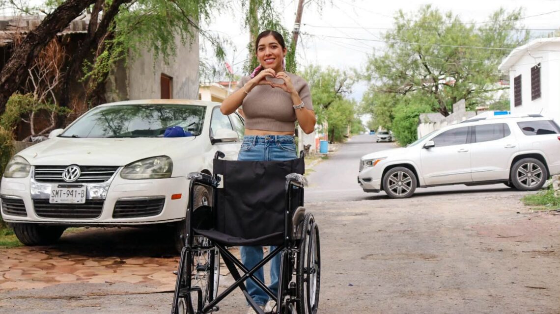 Perla Cavazos durante una visita a una familia de Ciénega de Flores, con una silla de ruedas y un gesto de corazón con las manos