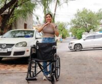 Perla Cavazos durante una visita a una familia de Ciénega de Flores, con una silla de ruedas y un gesto de corazón con las manos